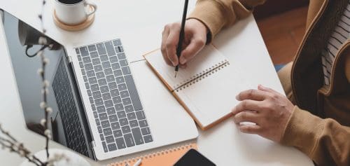 Cropped shot of male freelancer working on his project while writing his ideas on notebook in comfortable workspace