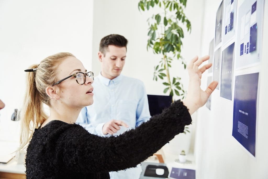 Two people looking at printed plans stuck on a wall, project management and discussions. ,Office,United Kingdom